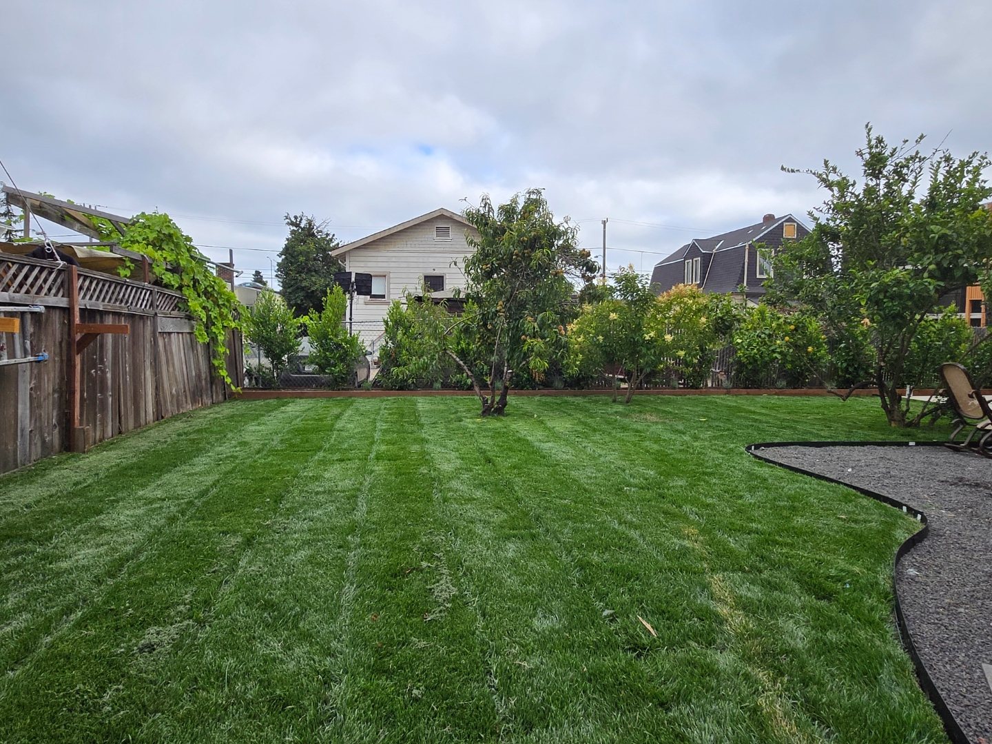 Large green backyard lawn bordered by trees and a gravel patio